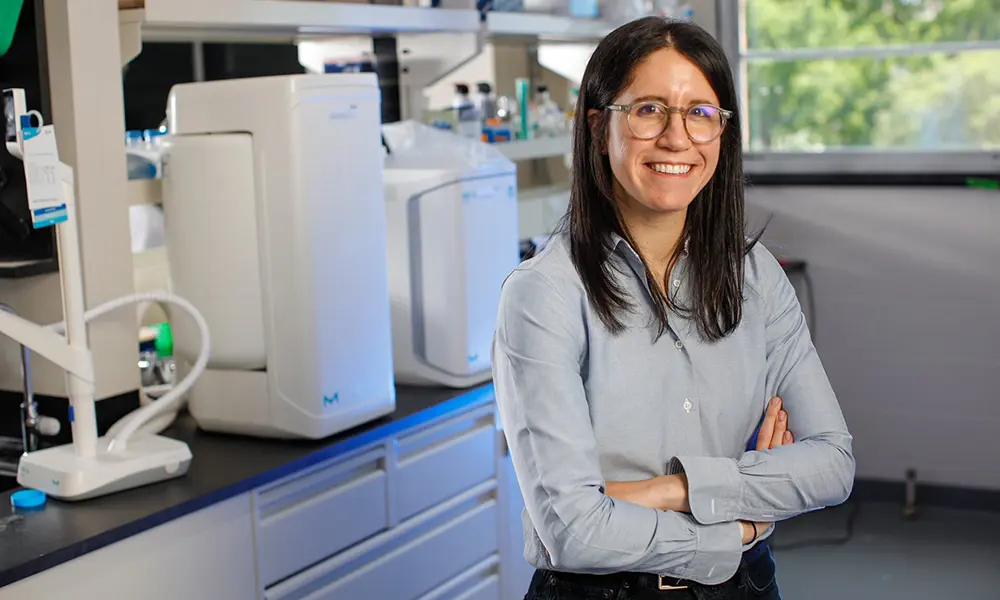 Allison Lopatkin stands with her hands crossed in front of some lab equipment.